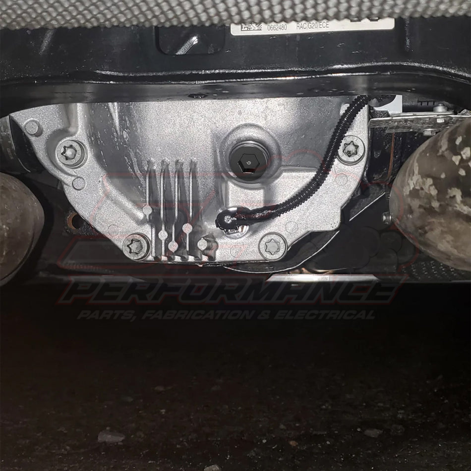 Underside view of BMW Mini differential drain plug 33117525064 installed in silver differential housing with mounting bolts and cooling fins visible