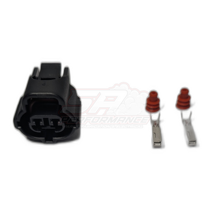 Black 2-pin Toyota IAT sensor connector housing shown from front angle with two metal terminals and red rubber seals laid out beside it