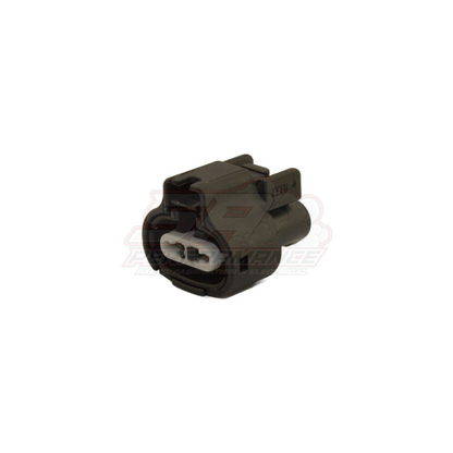 Black 2-pin Toyota Denso push-in connector housing with white terminal insert, angled view showing mating face and locking tabs